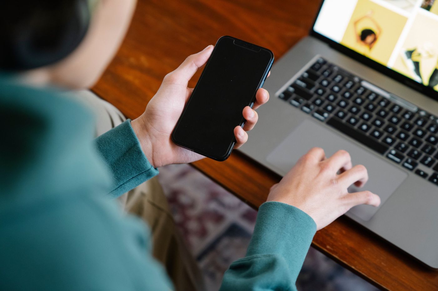 A Person Using a Laptop while Holding a Smartphone · Free Stock Photo